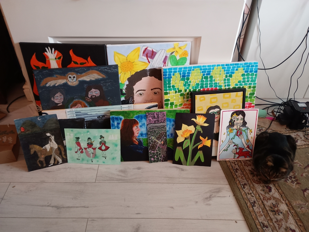 All twelve of the paintings that I did that have been documented on this blog, laid next to eachother by an old fireplace. A small tabby cat sits to the side