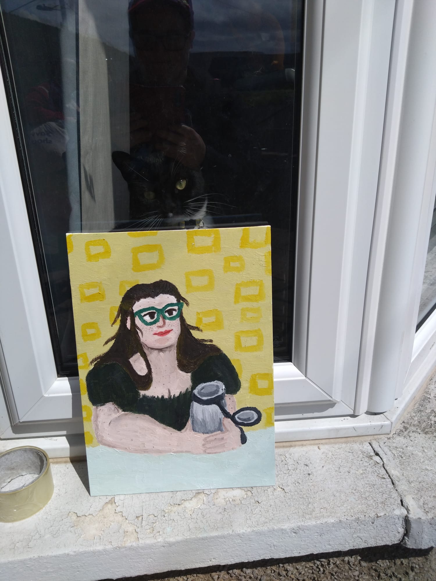 My painting leant against a windowsill, inside the window is the head of a black and white cat