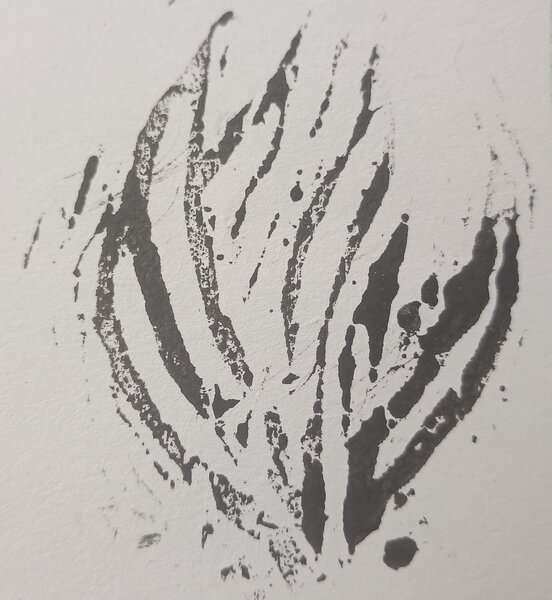 A woodblock with a carved heart, grass, a gate and blossom in different parts. These are all painted black (seeming almost stained)